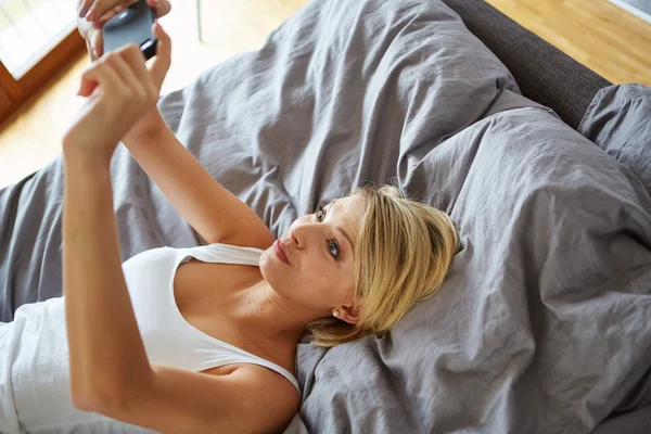 Женщина лежит на кровати и делает селфи — стоковое фото