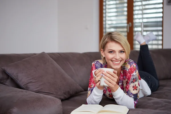 Mujer disfrutando leyendo un libro en casa tumbada en el sofá — Foto de Stock