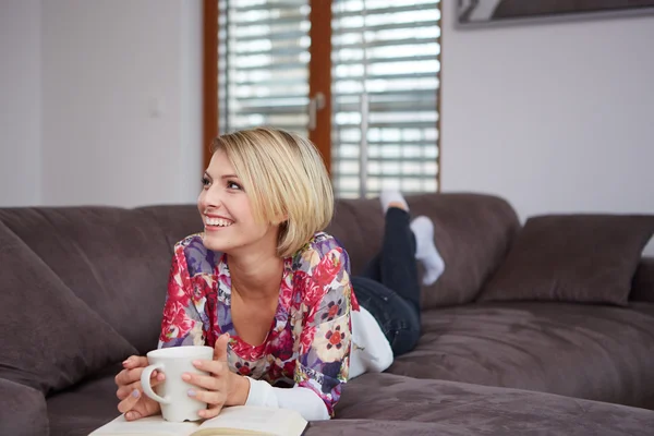 Kvinna som njuter av att läsa en bok hemma liggande på soffan — Stockfoto