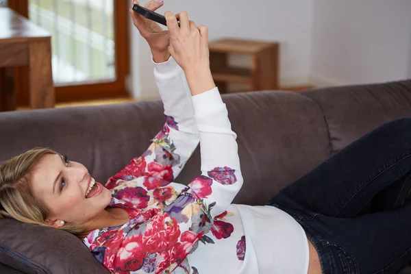 Mujer atractiva sentada en un acogedor sofá en la luminosa sala de estar con una llamada telefónica — Foto de Stock