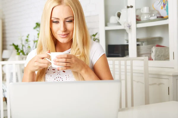 Donna carina che beve una tazza di tè mentre usa il suo computer portatile — Foto Stock