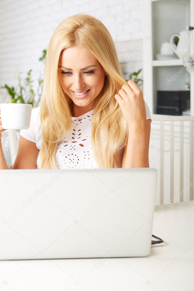Cute woman having a cup of tea while using her laptop 