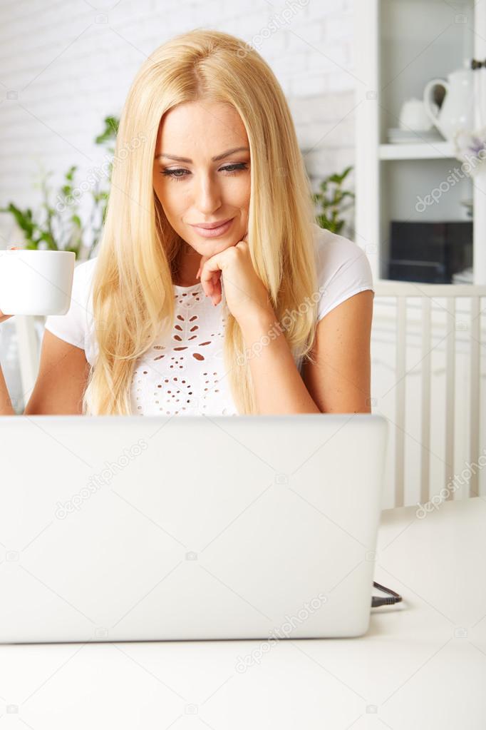 Cute woman having a cup of tea while using her laptop 