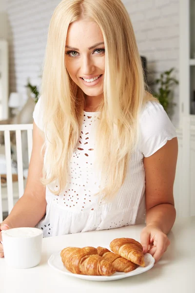 Vackra unga blonda kvinnan njuter av en färsk frasig croissant — Stockfoto