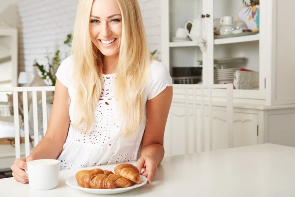 Hermosa joven rubia disfrutando de un croissant crujiente fresco —  Fotos de Stock