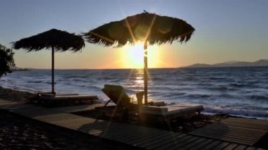 Gün batımında Kos sahilinde palmiye yaprakları ve güneş yataklarından yapılmış şemsiyeler..
