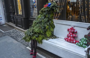 LVIV, UKRAINE - 14 Aralık 2019: Siyah taytlı ve kırmızı ayakkabılı kadınların bacakları beyaz bankta oturan şık bir Noel ağacı. orijinal yeni yıl dekorasyonu