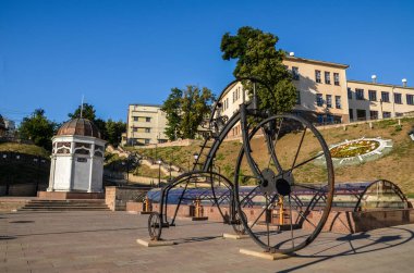 CHERNIVTSI, UKRAINE - 09 Ağustos 2015: Avusturya büyük demir bisiklet heykeli, Türk kuyusu ile Aziz Maria 'nın tarihi meydanında çiçek saati.