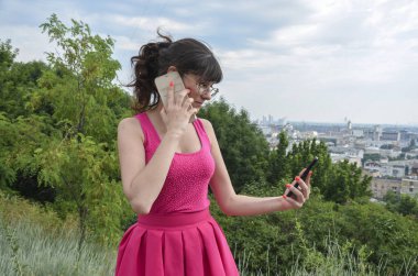 Pembe elbiseli çekici bir kız telefonda konuşuyor ve aynı anda ikinci telefona bakıyor. Çoklu görev ve popüler konsept