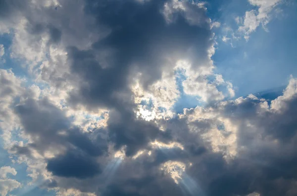 Blue sky with white and gray clouds and sun rays.  Different depth of color and shadow