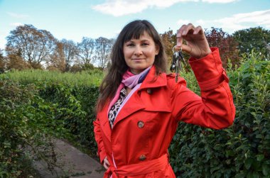 Şirin, gülümseyen esmer kız elinde kamerayla evin anahtarlarını gösteriyor. Emlakçı fikri