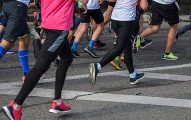 Aktif koşan bir grup insan, şehir yolunda koşan maraton koşucuları, bacakların detayları. Arka plan.