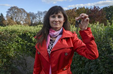 Şirin, gülümseyen esmer kız elinde kamerayla evin anahtarlarını gösteriyor. Emlakçı fikri