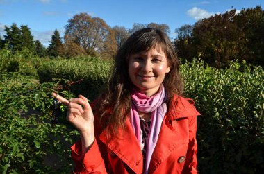 Kırmızı ceketli mutlu esmer kadın gülümsüyor ve elinde anahtarlar var. Araba ya da ev kirası