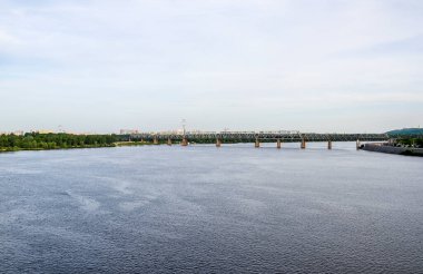 Petrivsky demiryolu köprüsü Kyiv 'deki Dnipro nehri üzerinde. Yazın bulutlu gökyüzüne karşı nehir boyunca endüstriyel çelik köprü