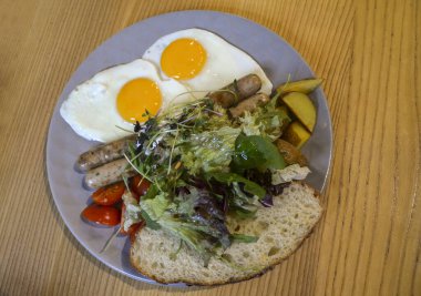 Kahvaltı için taze salata, patates ve ekmek ile bir tabak kızarmış yumurta ve kızarmış sosis.