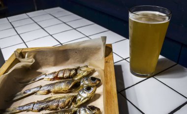 Bir kupa nefis bira ve masadaki parşömen kağıdında beş kurutulmuş balık. Seçici odak