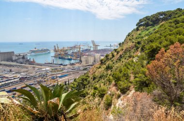 View of Barcelona cargo port at the Mediterranean Sea with cranes loading docks and and containers from the Montjuic mountain. Industrial port for freight transport and global business. 
