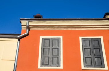Ukrayna 'nın Lviv şehrinin tarihi bölgesinde, mavi gökyüzünün altında iki penceresi ve kapalı panjurları olan kırmızı boyalı bir duvar.