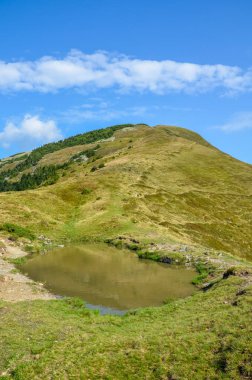 Güzel dağ manzarası, mavi gökyüzünde bulutlar yüksek yeşil tepeler, kayalar ve göl. Karpatlar, Ukrayna