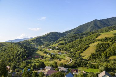 Tepelerdeki köy evleri ve vadideki yeşil çayırlar ile Karpat Dağları manzarası