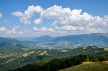 Yükseklikten manzara çok güzel. Vadideki tipik Karpatlar köyü, beyaz bulutlu mavi gökyüzünün altındaki orman ve dağlar. Karpatlar, Ukrayna