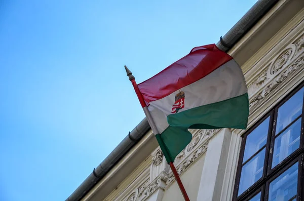 Hungarian flag on a flagpole waving in the wind from building on a sunny day.