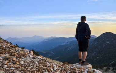 Arkadan bak. Yalnız bir adam dağların tepesinde durup gün batımını seyreder. Turizm seyahati kavramı. Tahtali dağı, Türkiye
