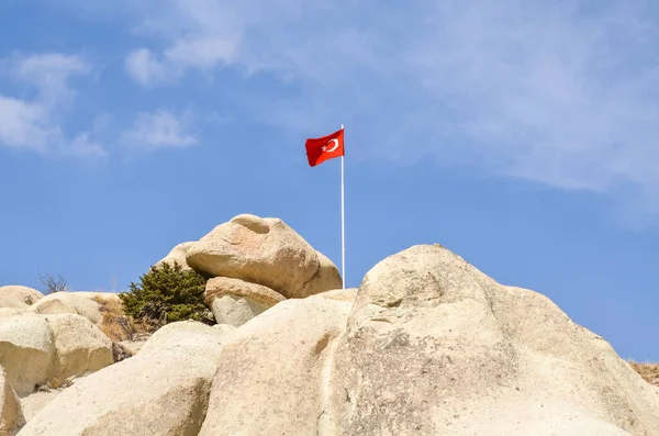 青い空を背景にカッパドキアの典型的な凝灰岩の岩の形成と丘の上のトルコ国旗 ゴーレム トルコ — ストック写真