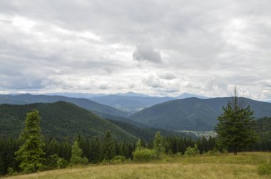 Karpatlar ormanı ve köyü kaplamış, arka planda dağ sırtı var. Karpatlar ve Ukrayna 'da bulutlu bir gün