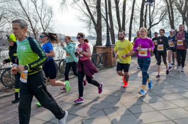 Spor kıyafetleri giyen çeşitli koşucular turuncu konileri geçen güneşli bir rıhtımda yarışıyorlar. Sahne fitness, takım çalışması ve açık hava dayanıklılığını yakalıyor.