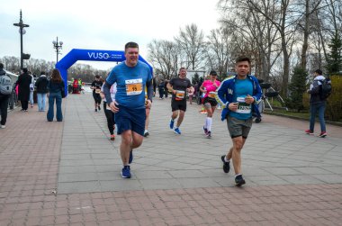 Halk parkı yarışında koşucular finiş çizgisine doğru koşarken, arka planda seyirciler tezahürat yapıyor.