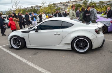 Gösterişli, beyaz modifiye Toyota GT86, geniş gövdeli ve siyah tekerlekli arka teker çekişli spor coupe hafif, dengeli şasisi ile bilinir.