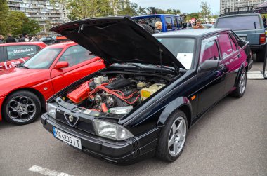 Alfa Romeo 75, siyah kapüşonlu dört kapılı bir sedan ve kabarık bir kaput, belirgin kama şekli ve siyah plastik entegre yan etekleri var.