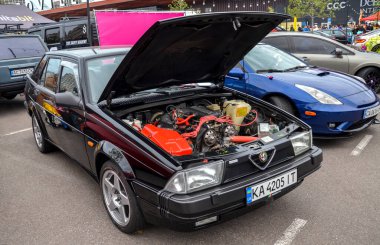 Alfa Romeo 75, siyah kapüşonlu dört kapılı bir sedan ve kabarık bir kaput, belirgin kama şekli ve siyah plastik entegre yan etekleri var.