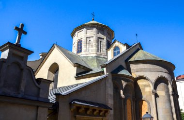 Stone Armenian Cathedral with multiple crosses, a central dome, and arched windows stands under a clear blue sky. Lviv, Ukraine