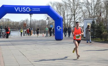 Erkek koşucu, açık bir günde izleyiciler rıhtım boyunca seyrederken büyük mavi şişme kemerin altında finişe doğru hızlanır.