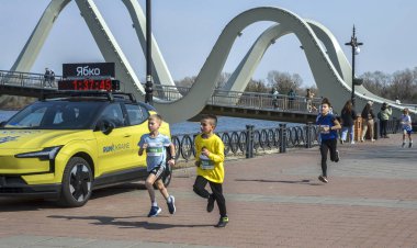 Çocuklar kemerli bir köprünün yanındaki rıhtım boyunca koşarlar. Enerjik ve sportif sahne, gündüz etkinliklerinde genç koşucuları ve toplum enerjisini yakalıyor