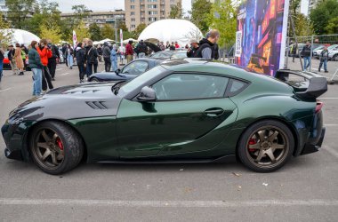 Siyah kapüşonlu, koyu yeşil Toyota Supra. İki kapılı spor araba. Uzun kapüşonlu ve şekillendirilmiş vücut hatları olan cesur, agresif bir tasarım.