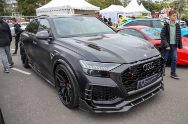 Koyu gri Audi RS Q8 özel vücut kiti ve turuncu iç aksanlı bir açık hava etkinliğinde park halinde.