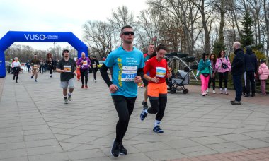 Koşucular, seyirciler tezahürat yaparken bir şehir caddesinde bitiş çizgisine doğru koşuyor. Açık hava yarışı enerji, kararlılık ve toplum ruhunu yakalar.