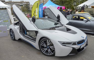 Çarpıcı beyaz BMW i8 hibrit spor araba ikonik makas kapıları ile sunuluyor. Gösterişli çizgiler ve mavi aksanların yer aldığı fütüristik ve aerodinamik tasarım vurgulandı