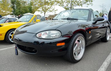 İkinci nesilden (NB) siyah Mazda MX-5 Miata, üstü açık, klasik spor arabasının cazibesini sergiliyor.