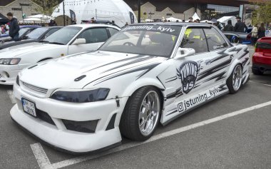 Büyük ölçüde modifiye edilmiş beyaz Toyota Mark II bir açık hava araba etkinliğinde belirgin bir şekilde sergilenmek üzere tasarlandı. JDM kültürü, drift yarışı, araba akordu, özel arabalar