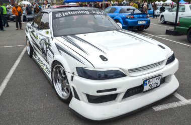 Büyük ölçüde modifiye edilmiş beyaz Toyota Mark II bir açık hava araba etkinliğinde belirgin bir şekilde sergilenmek üzere tasarlandı. JDM kültürü, drift yarışı, araba akordu, özel arabalar