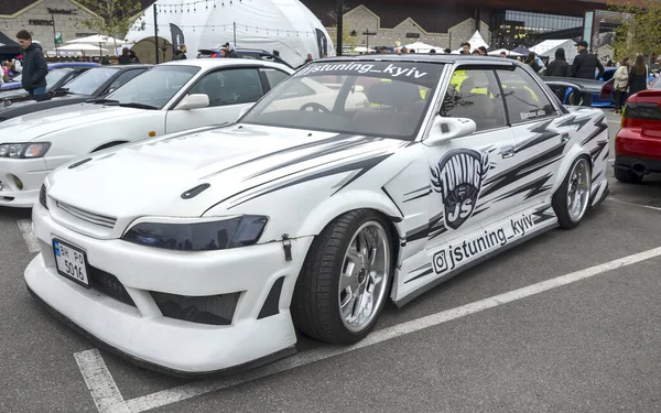 Büyük ölçüde modifiye edilmiş beyaz Toyota Mark II bir açık hava araba etkinliğinde belirgin bir şekilde sergilenmek üzere tasarlandı. JDM kültürü, drift yarışı, araba akordu, özel arabalar