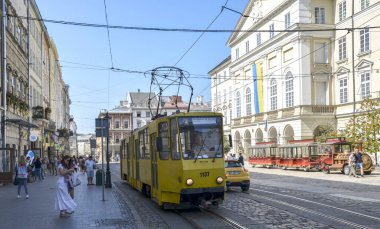 Parlak sarı tramvay güneşli bir günde tarihi binalar ve yayalarla dolu bir pazar meydanından geçiyor. Lviv, Ukrayna