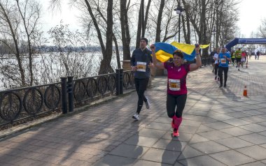 Koşucular nehir kenarındaki bir geçitte kutlama yapıyorlar. Bir kadın zaferle mavi ve sarı bayrak kaldırıyor. Neşeli kalabalıklar, ve parlak, güneşli bir gün sahneyi hazırladı