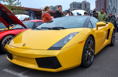 Canlı sarı Lamborghini Gallardo Spyder, gösterişli çizgileri, siyah yumuşak bluzu ve görünür performans tekerlekleri olan sembolik bir İtalyan spor arabası.