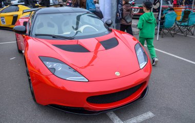 Çarpıcı kırmızı Lotus Evora spor arabası açık havada sergileniyor, özel ön ızgarası, parlak farları ve siyah bir çatısı var.